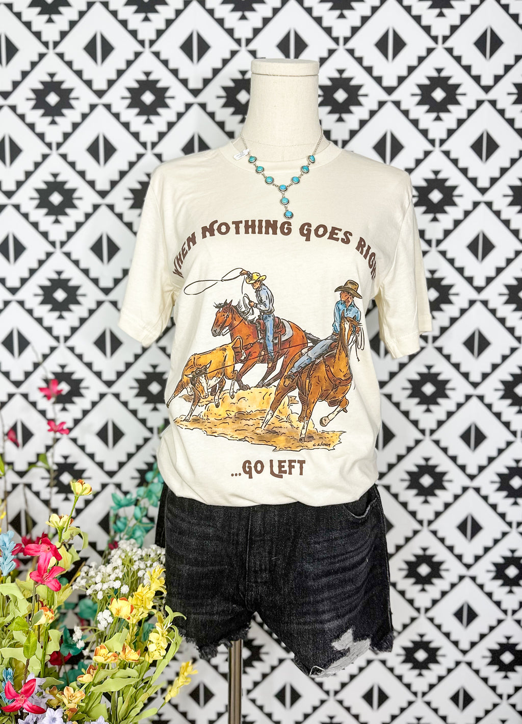Creams colored graphic t shirt with a team roping graphic that reads When nothing goes right, go left.”
