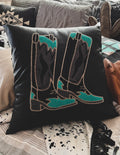 A decorative pillow case with a black background featuring an embroidered design of boots in teal and grey colors. 
