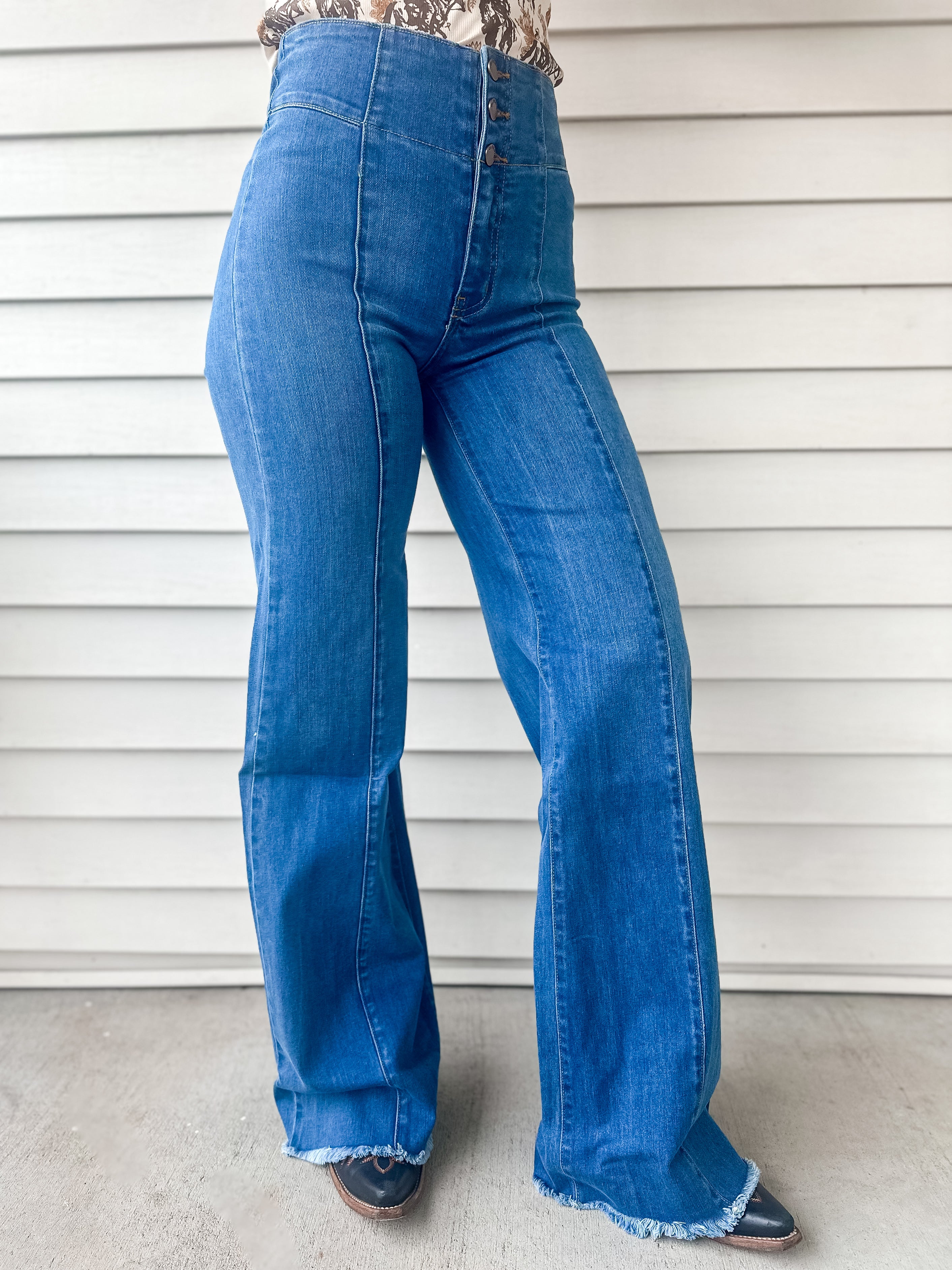 High waisted medium wash wide leg trouser style jeans with 3 button and zipper closure long inseam and raw hem with front seam and no pocket design 