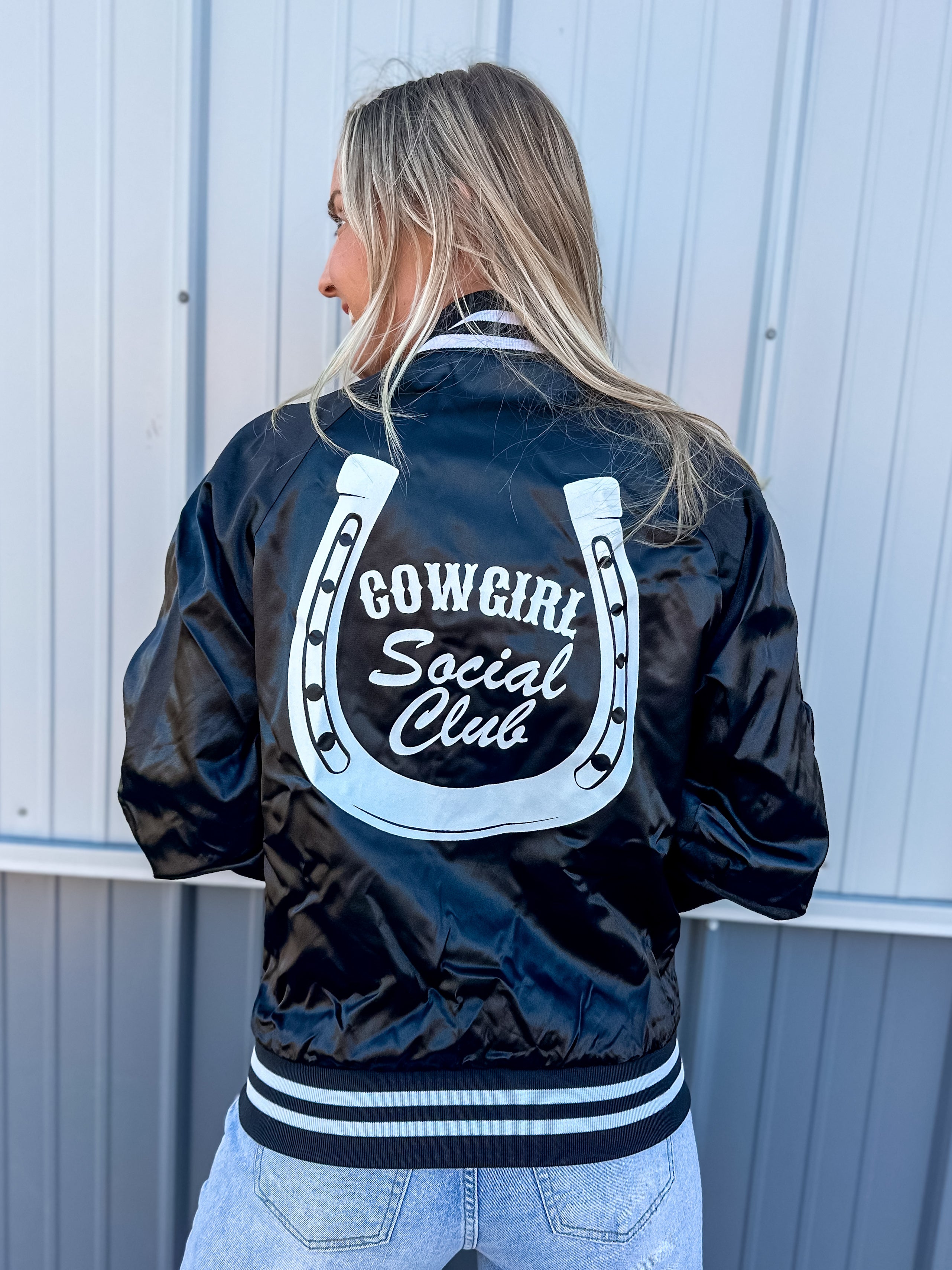 Black 'Cowgirl Social Club' varsity jacket with white text and horshoe logo on the back.