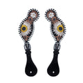 A pair  tooled leather spur straps with a floral pattern in yellow, white, and black colors, and a dash of brown.